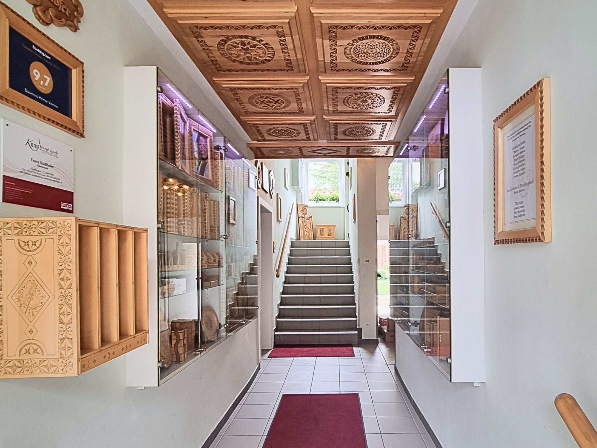A hallway with a wooden staircase, glass display cases, and framed certificates on the walls.