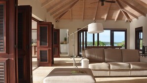 Un salon spacieux avec un plafond haut, une grande fenêtre donnant sur l’extérieur, un canapé beige et un lampadaire.