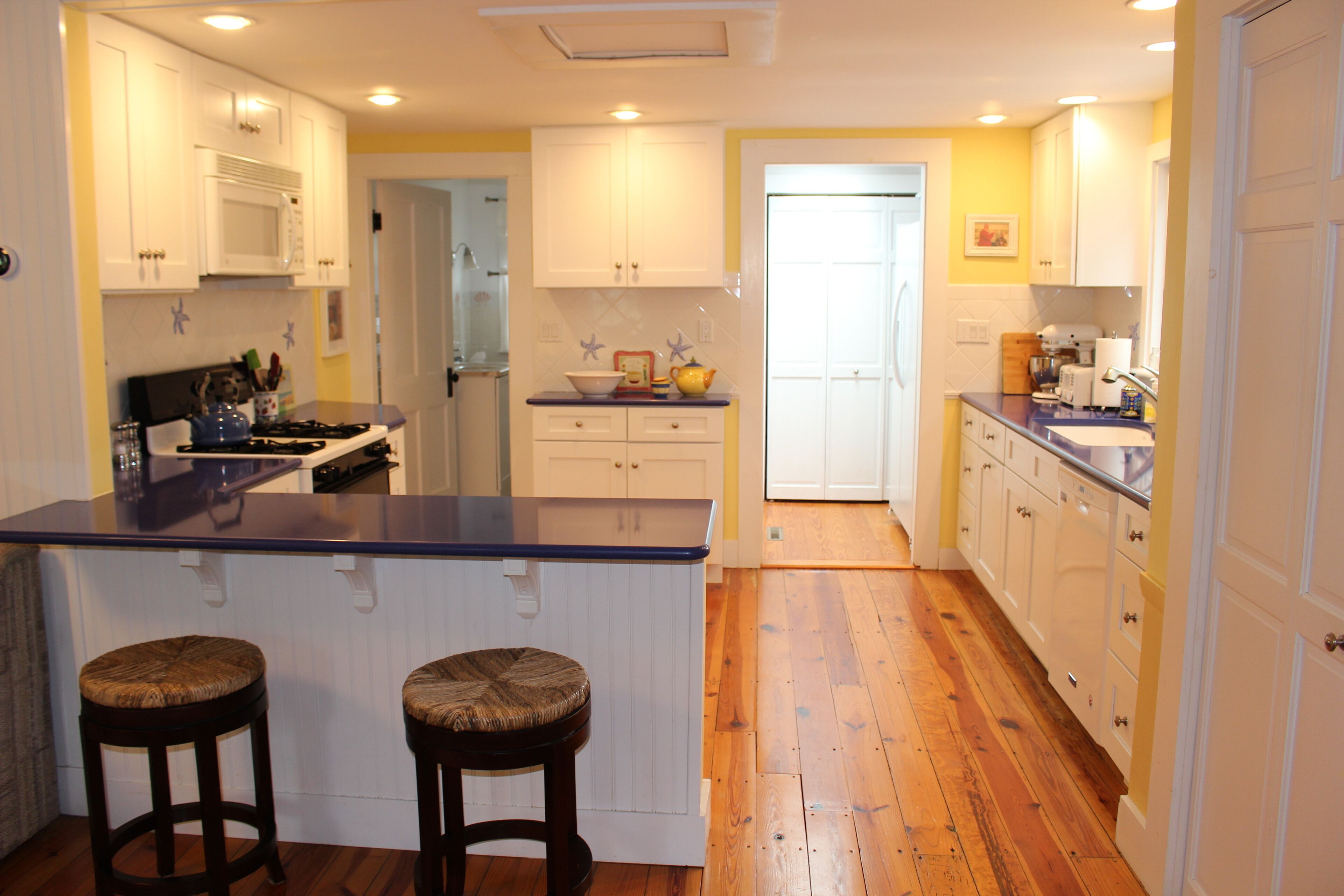 A kitchen with wooden flooring, white cabinets, a blue countertop, and two stools.