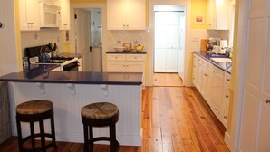 A kitchen with wooden flooring, white cabinets, a blue countertop, and two stools. - Spacious, Private Cape Cod Cottage with Central Air (Harwich Port)