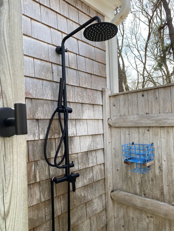 Une douche d’extérieur noire, dotée d ’un pommeau de douche à effet pluie, fixée sur un mur en bois.
