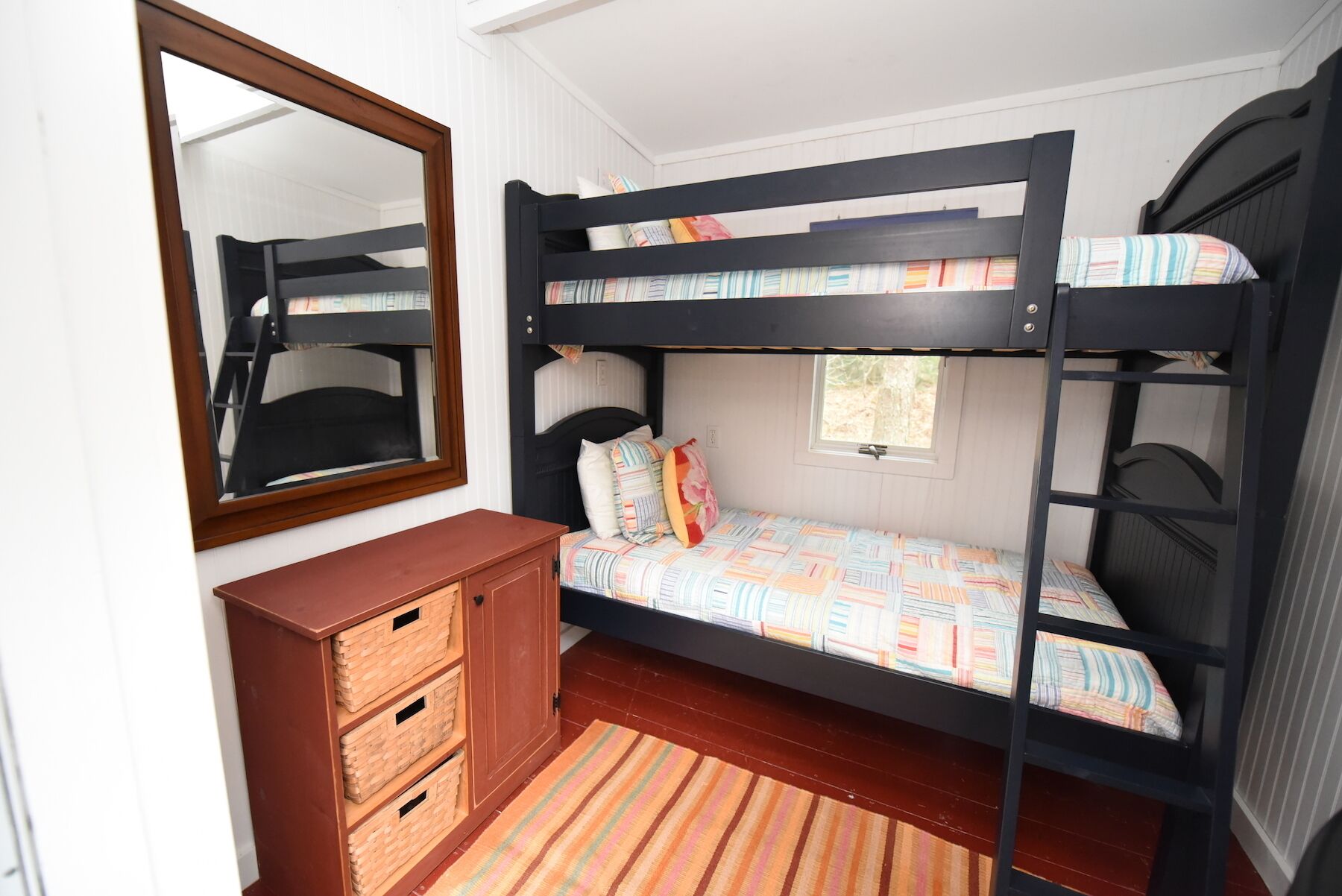 A bunk bed room with a wooden dresser and a mirror.