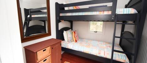 A bunk bed room with a wooden dresser and a mirror.