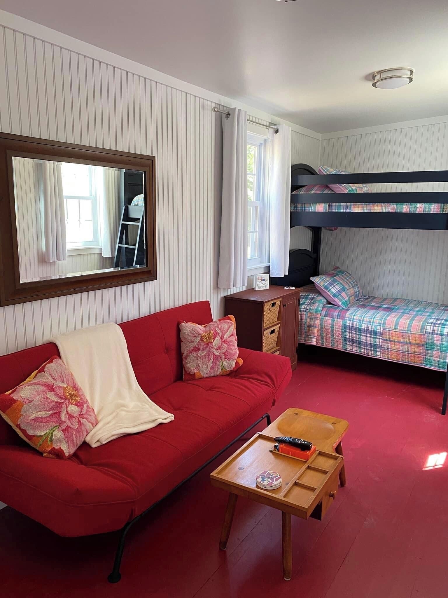 A room with a red sofa, a wooden table, a bunk bed, and a mirror on the wall.