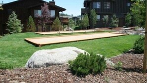 Une pelouse bien entretenue, agrémentée d’un long banc en bois, d’un grand rocher et d’un petit arbuste.