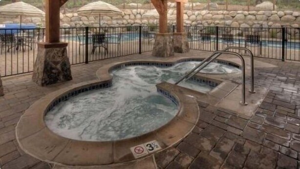 Un espace avec un jacuzzi, des piliers en pierre et une piscine entourée d’une clôture.