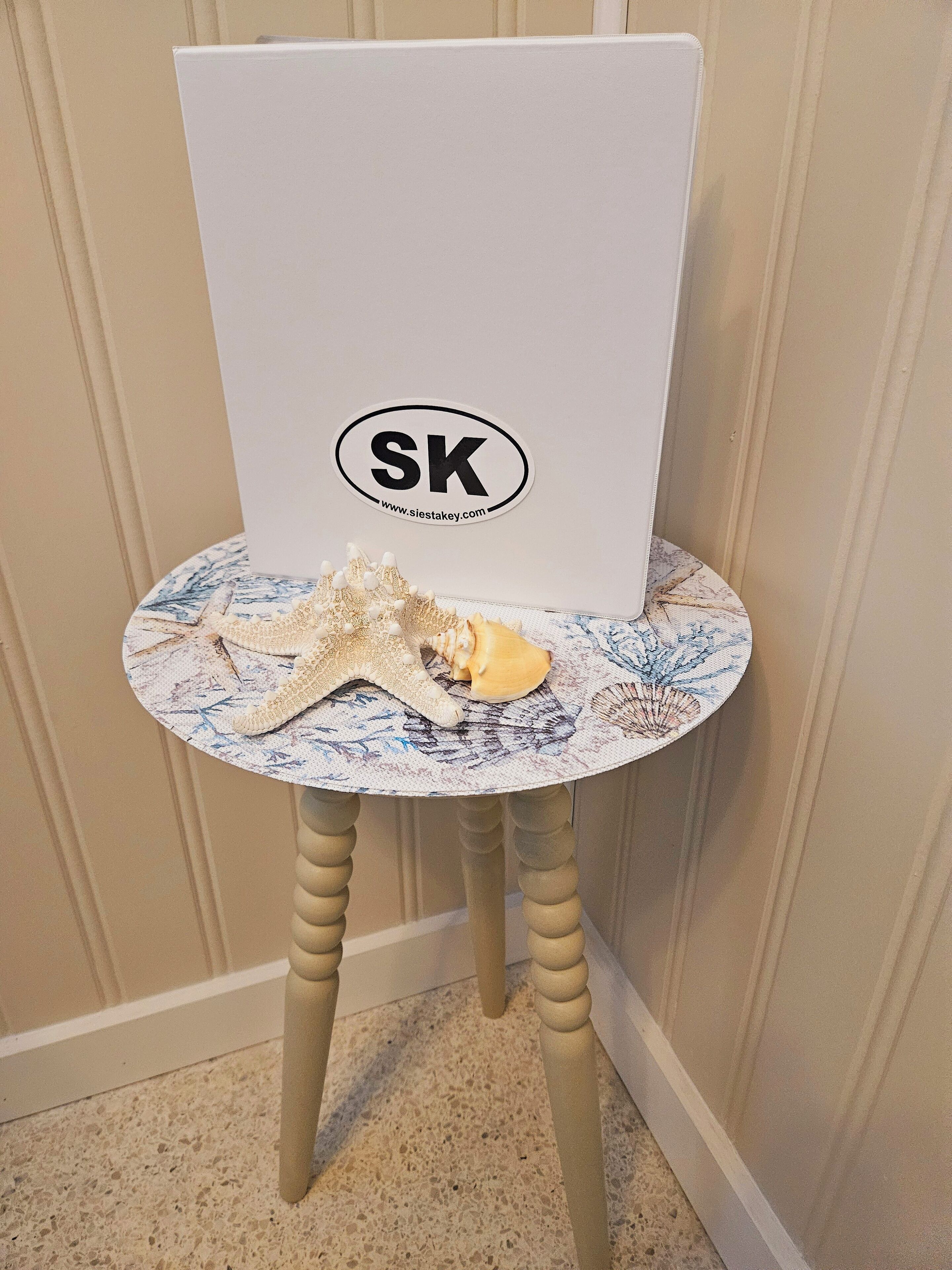 A white chair with a round table featuring a seashell and starfish decoration.