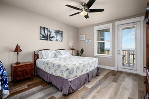 A bedroom with a bed, a nightstand, a ceiling fan, and a door with a window.
