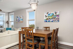 A dining area with a wooden table and chairs, a white sofa, and two paintings on the wall.