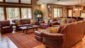 A spacious living room with leather sofas, a wooden coffee table, and large windows offering a view of the outdoors. - Premier Luxury Home with 7 BR/7.5 BA, Hot Tub, Game Room, SHARC passes, A/C (Sunriver)