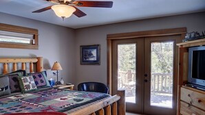 A bedroom with a wooden bed, a ceiling fan, a television, and a sliding glass door leading to an outdoor area. - Premier Luxury Home with 7 BR/7.5 BA, Hot Tub, Game Room, SHARC passes, A/C (Sunriver)