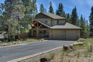 Stunning two-story home with a gabled roof and inviting front porch, set amidst a serene natural landscape.