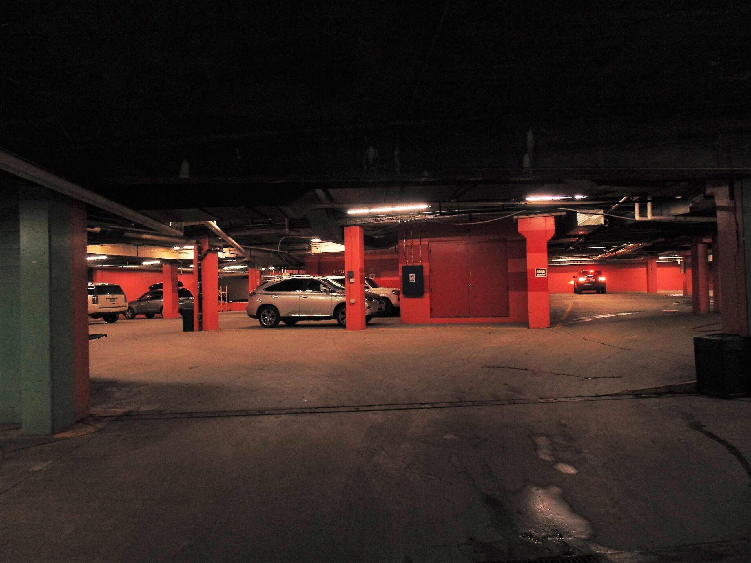 A parking garage with red pillars and a white car parked in the foreground.