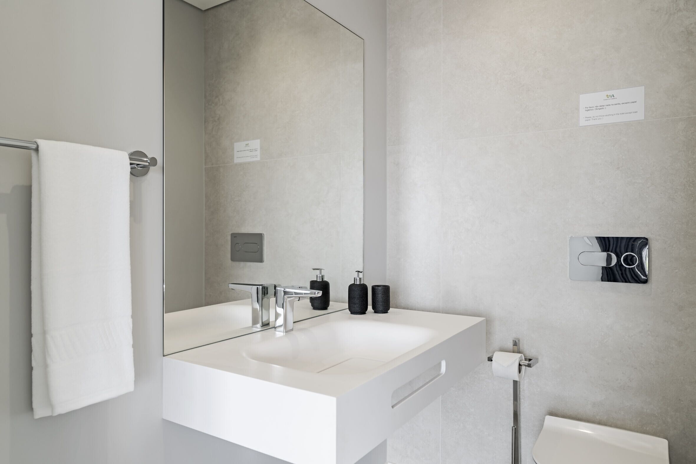 Ein modernes Badezimmer mit großem Spiegel, weißem Waschbecken und Handtuchhalter.