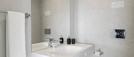 Ein modernes Badezimmer mit großem Spiegel, weißem Waschbecken und Handtuchhalter.