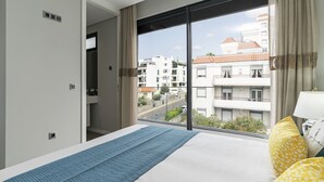 Habitación de hotel con una cama grande, vista a la ciudad por una ventana y puerta que da a un espacio al aire libre.