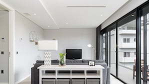 Una sala de estar moderna con una consola blanca, un sofá gris y un amplio ventanal con vistas a la ciudad.