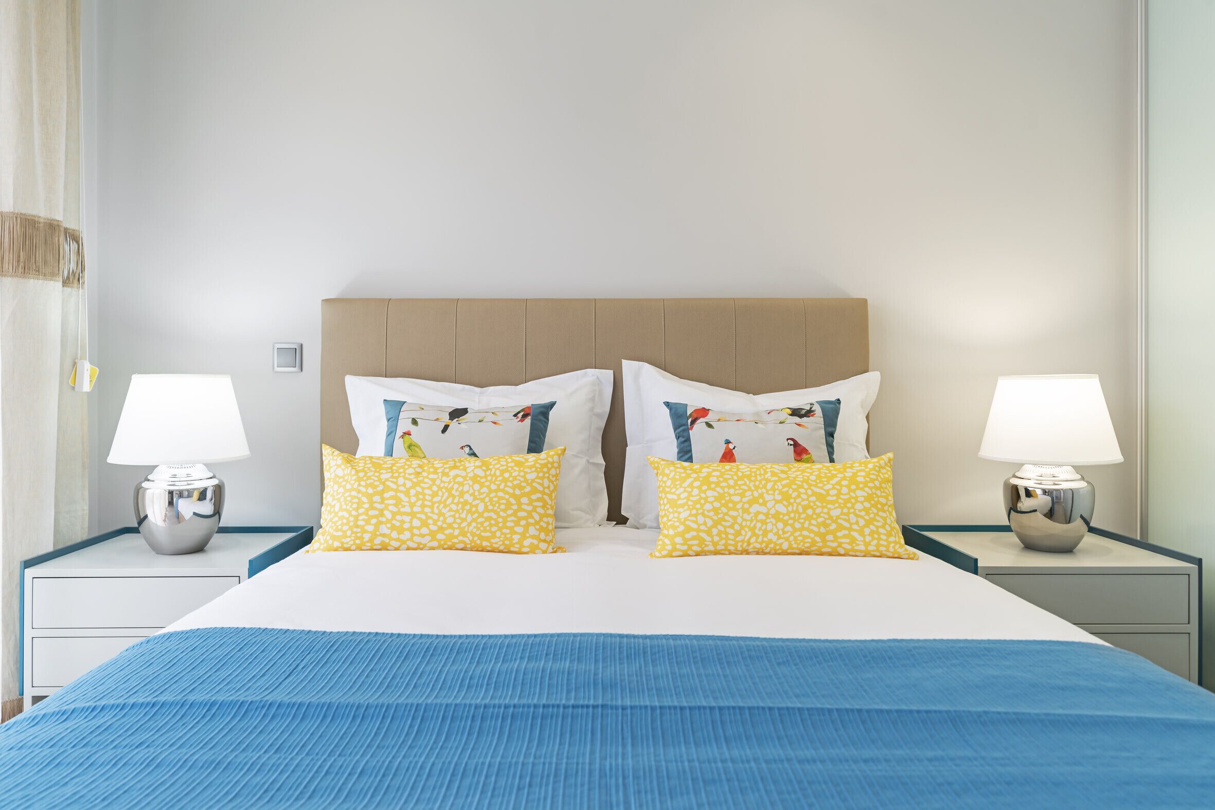 A hotel room with a large bed, two bedside tables with lamps, and a headboard with a bird pattern.