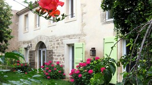 Edificio de piedra con jardín delantero, con flores rosas y hojas verdes.