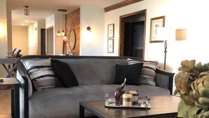 Ein modernes Wohnzimmer mit grauem Sofa, einem Couchtisch und einem Essbereich mit Tisch und Stühlen.