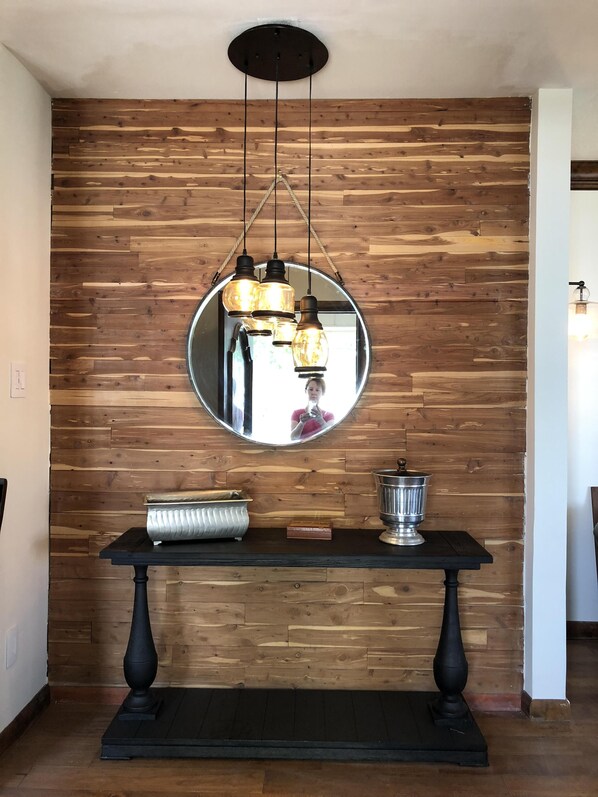 A wooden wall with a round mirror, a black table with a metal container, and a hanging light fixture.