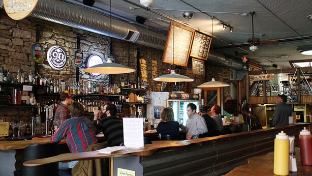 Eine Bar mit einer Steinwand, verschiedenen Spirituosenflaschen und hängenden Schildern.