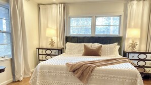 Ein ordentlich eingerichtetes Schlafzimmer mit einem großen Bett, zwei Nachttischen und einem Fenster mit Vorhängen.