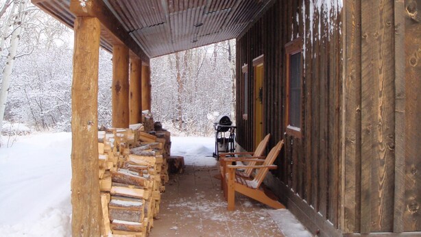 Eine Holzhütte mit überdachter Veranda, einem Sessel und einem Holzstapel.
