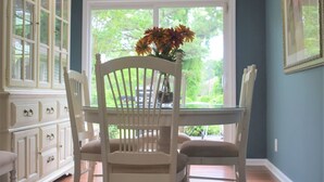 A dining area with a table and chairs, a window with a view of greenery, and a cabinet with drawers. - Moonshine Cottage - Time to GOLF! (Pinehurst)