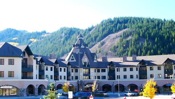 A hotel with multiple floors, a central tower, and a mountain backdrop. - In the heart of Avon -walk to restaurants & gondola!  Immaculate 2bed/2bath (Avon)