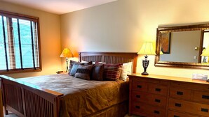 A bedroom with a wooden bed, a nightstand, a dresser with drawers, a mirror, and a window with blinds. - In the heart of Avon -walk to restaurants & gondola!  Immaculate 2bed/2bath (Avon)