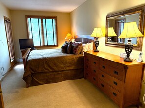 A hotel room with a bed, bedside lamps, a dresser, a television, and a window with blinds. - In the heart of Avon -walk to restaurants & gondola!  Immaculate 2bed/2bath (Avon)