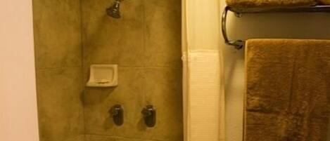 A bathroom with a bathtub, shower, and toilet. There are towels on a rack and a soap dish on the wall.