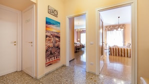 Un corridoio con pavimento in terrazzo, un quadro che raffigura una veduta cittadina, e un letto con lenzuola a righe nella stanza adiacente.