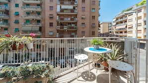Un balcone con piante in vaso, un tavolino rotondo e una sedia bianca.