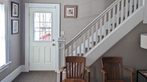 Una escalera con barandillas blancas, una puerta con ventana y dos sillas de madera.