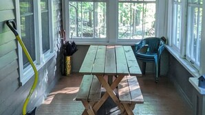 Un porche cubierto con una mesa y bancos de madera, rodeado de amplias ventanas con vistas al bosque.