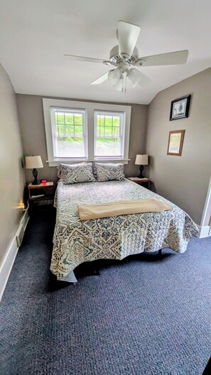 A bedroom with a bed, two bedside lamps, a ceiling fan, and two windows with blinds. - RARE FIND - Your Own Path to Lake Erie — Historic 5-Acre Lakefront Retreat (East Springfield)