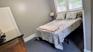 Un dormitorio con una cama, una mesita de noche, una lámpara y una ventana con persianas.