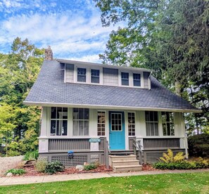 A two-story house with a blue front door, a covered porch, and a stone chimney. - RARE FIND - Your Own Path to Lake Erie — Historic 5-Acre Lakefront Retreat (East Springfield)