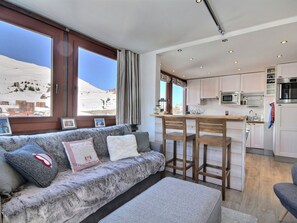 A living room with a sofa, a coffee table, and a view of a snowy landscape through large windows. - Renovated apartment 64m², 6 pers, balcony, Wi-Fi, slopes (La Plagne)