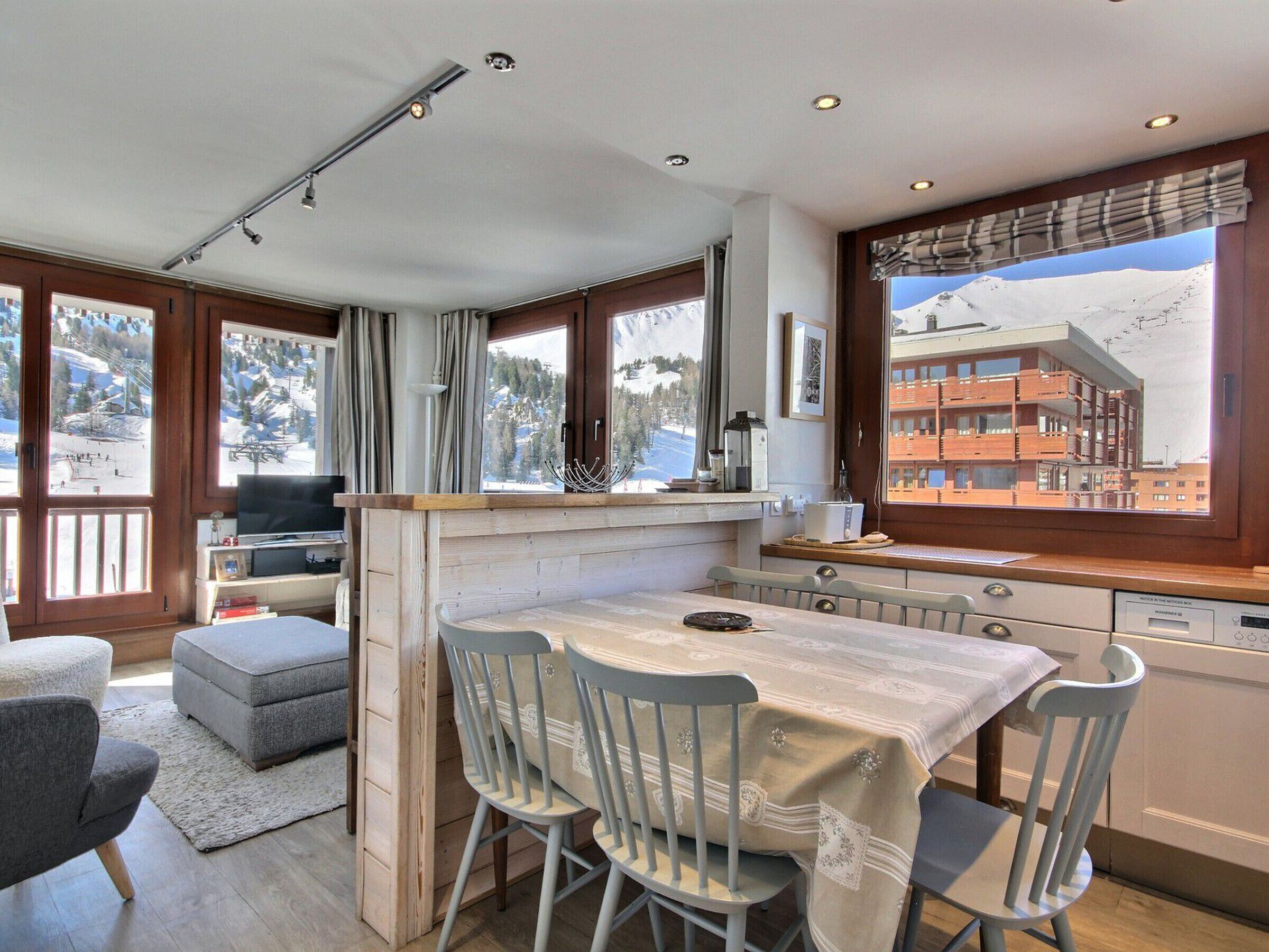 A modern kitchen with a dining area, large windows with mountain views, and a cozy seating arrangement.