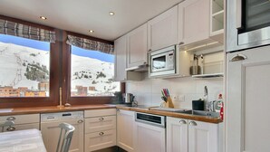 A kitchen with white cabinets, a microwave, a coffee maker, and a view of a snowy landscape. - Renovated apartment 64m², 6 pers, balcony, Wi-Fi, slopes (La Plagne)