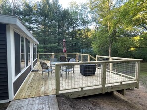 Eine Holzterrasse mit Gartenmöbeln, einem überdachten Tisch und einem eingezäunten Bereich.