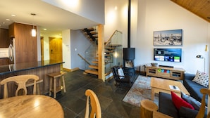 A modern living room with a fireplace, a TV mounted on the wall, and a wooden staircase.