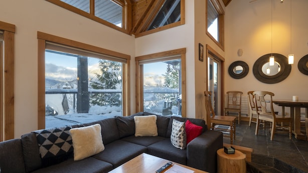 A cozy living room with a sectional sofa, wooden coffee table, and a view of snowy mountains through large windows.