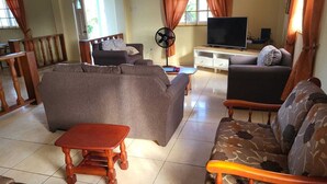 Un salon comprenant un canapé, un fauteuil, une table basse en bois, un téléviseur et un ventilateur.