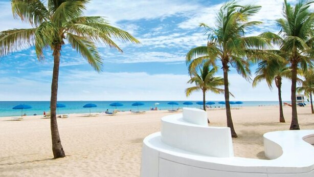 Una playa con palmeras, sombrillas azules y una orilla arenosa.