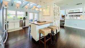 Una cocina amplia con una isla central, taburetes de bar y vistas al exterior a través de grandes ventanales.