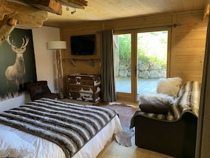 A wooden cabin bedroom with a bed, a dresser, a television, and a large window.